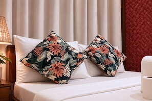 A hotel room with a bed, two decorative pillows with a tropical leaf pattern, a bedside lamp, and a red woven wall panel.