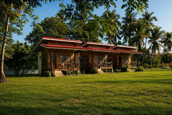 A two-story house with a red roof, surrounded by a well-maintained lawn and palm trees.