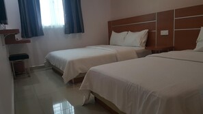 Habitación de hotel con dos camas individuales, un escritorio pequeño y una ventana con cortinas.