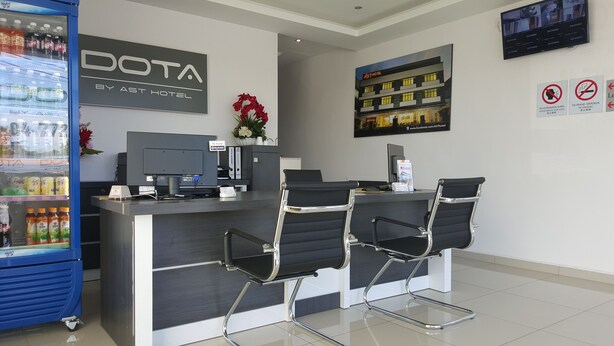 A reception area with a counter, two black office chairs, a computer, a beverage dispenser, and a wall-mounted TV. - DOTA Hotel (Alor Setar)