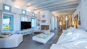 Un salón moderno con televisor de pantalla plana, sofás blancos, una mesa de centro de vidrio y un panel de pared de madera.