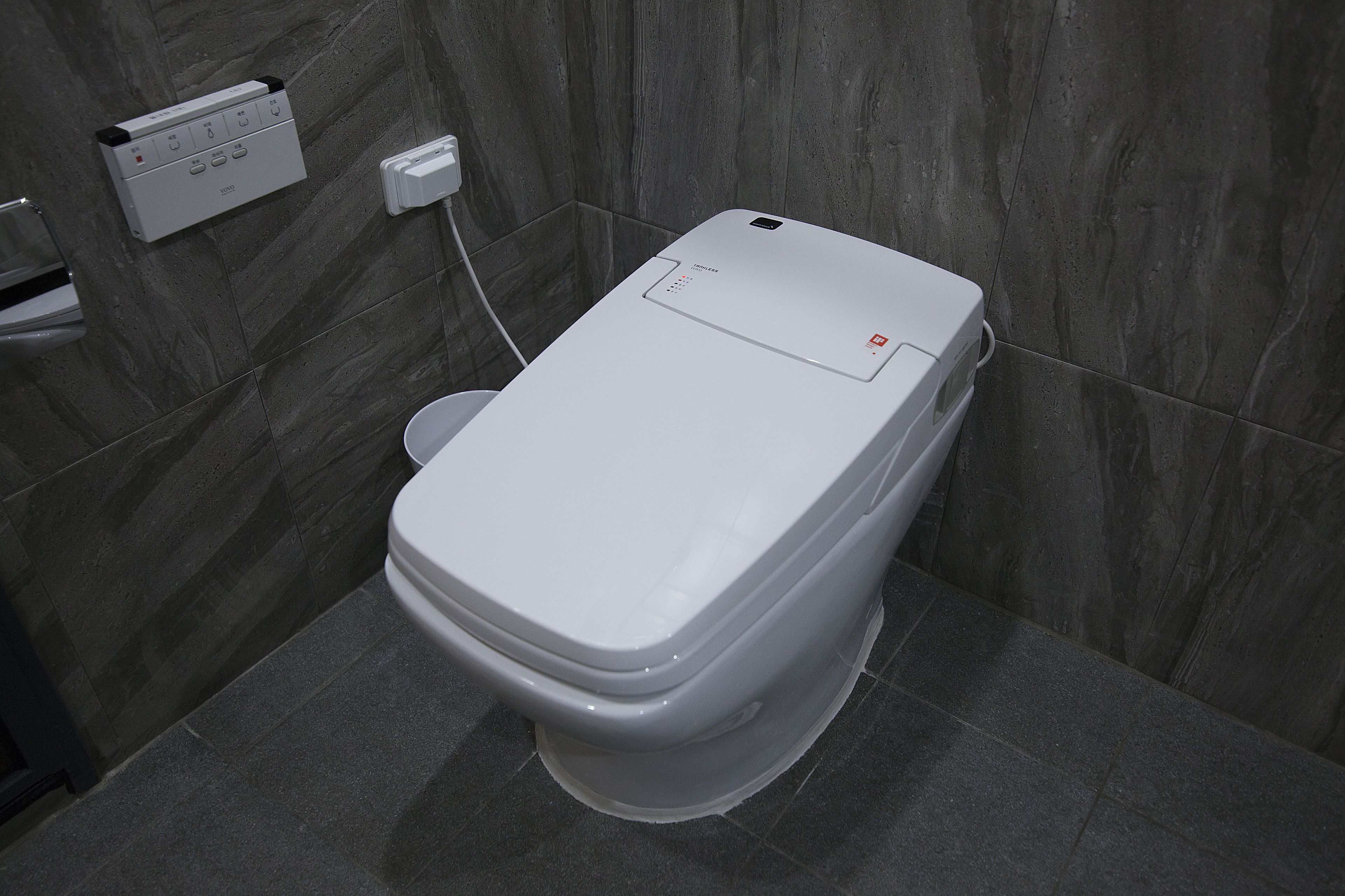 A modern toilet with a control panel and a wall-mounted flush button.