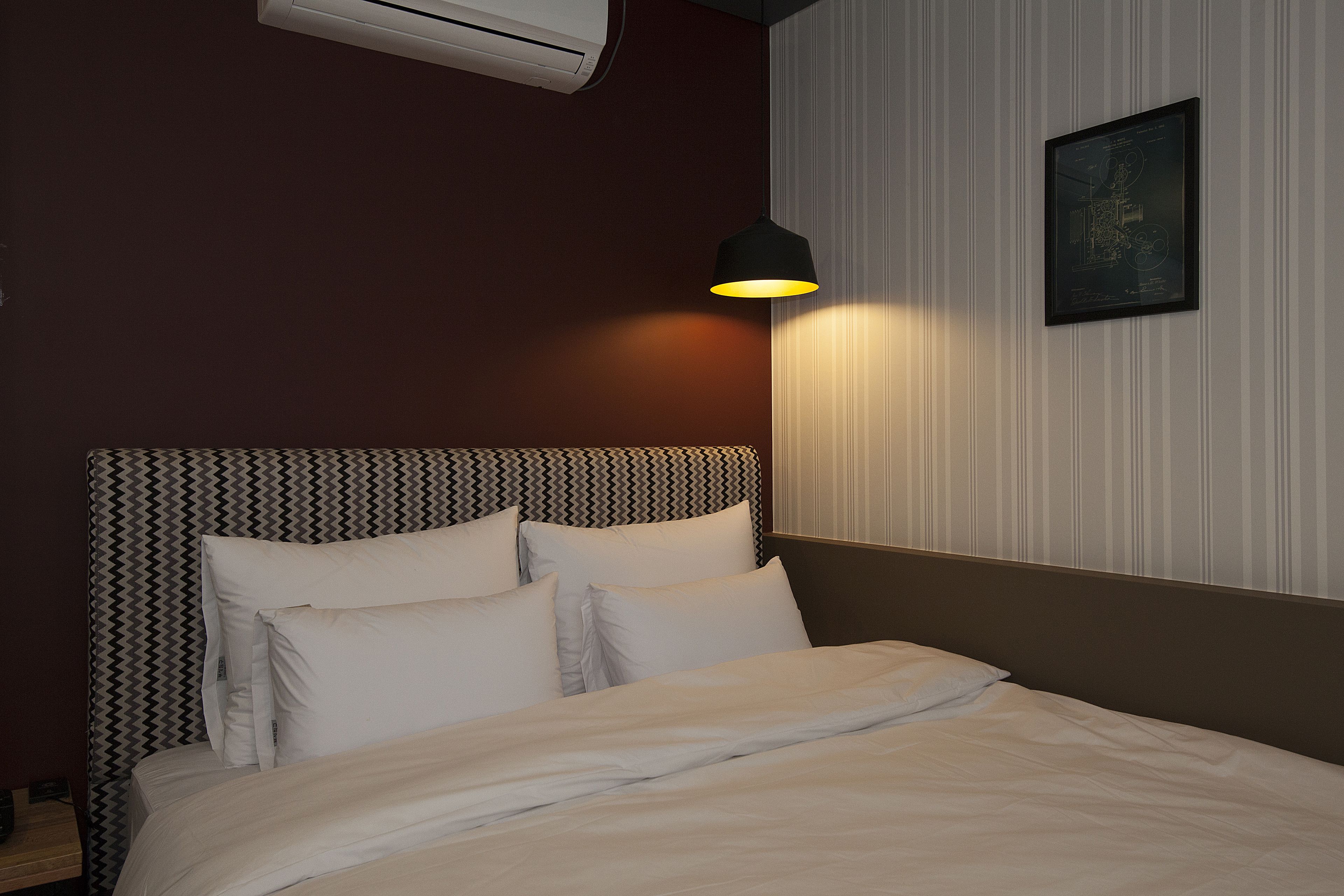 A neatly made bed with white linens, a headboard with a zigzag pattern, and a wall-mounted air conditioner.