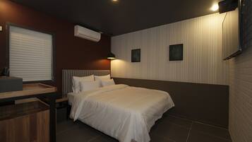 A hotel room with a bed, bedside table, and a window with blinds.