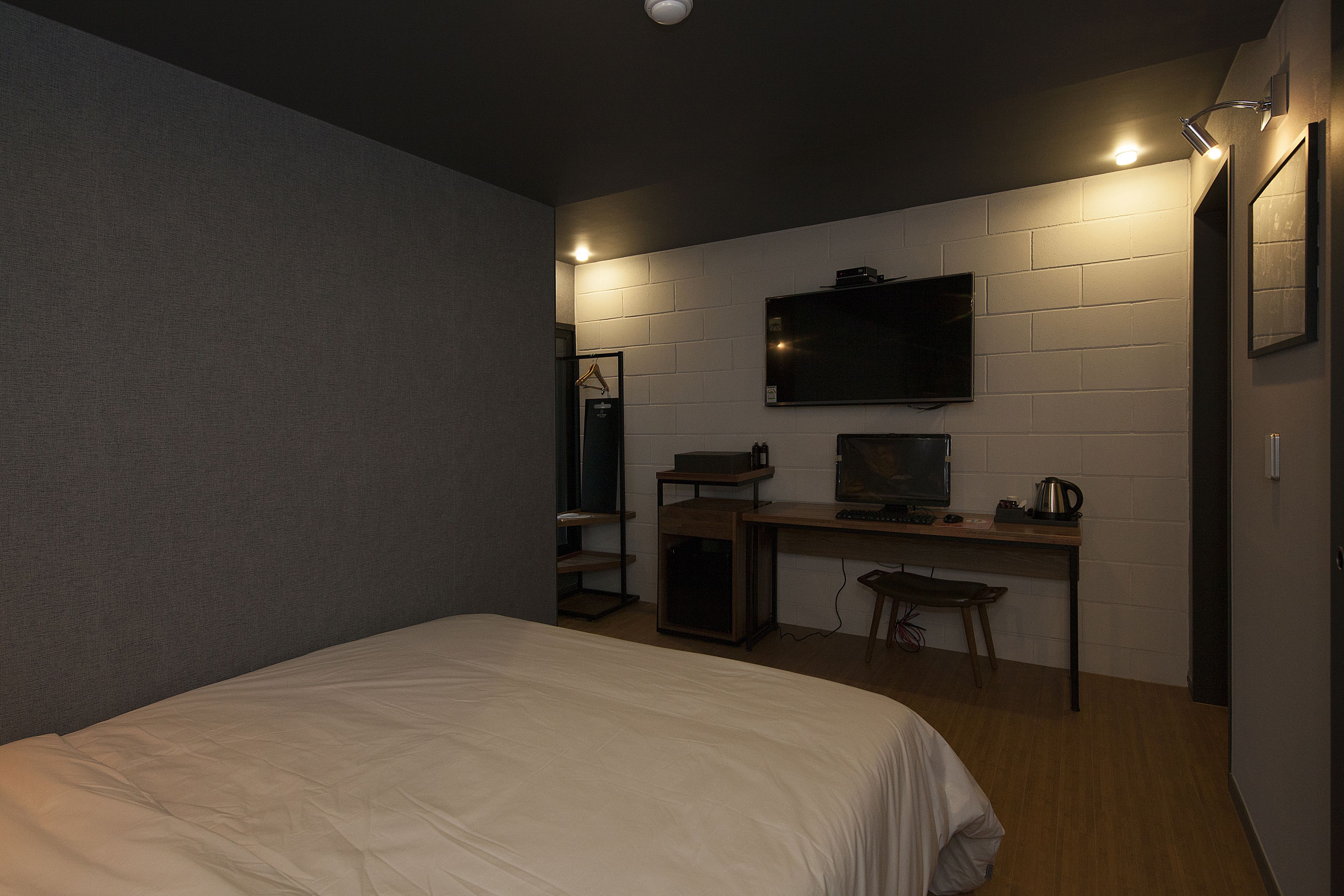 A bedroom with a bed, a desk with a computer, a TV, and a small cabinet.