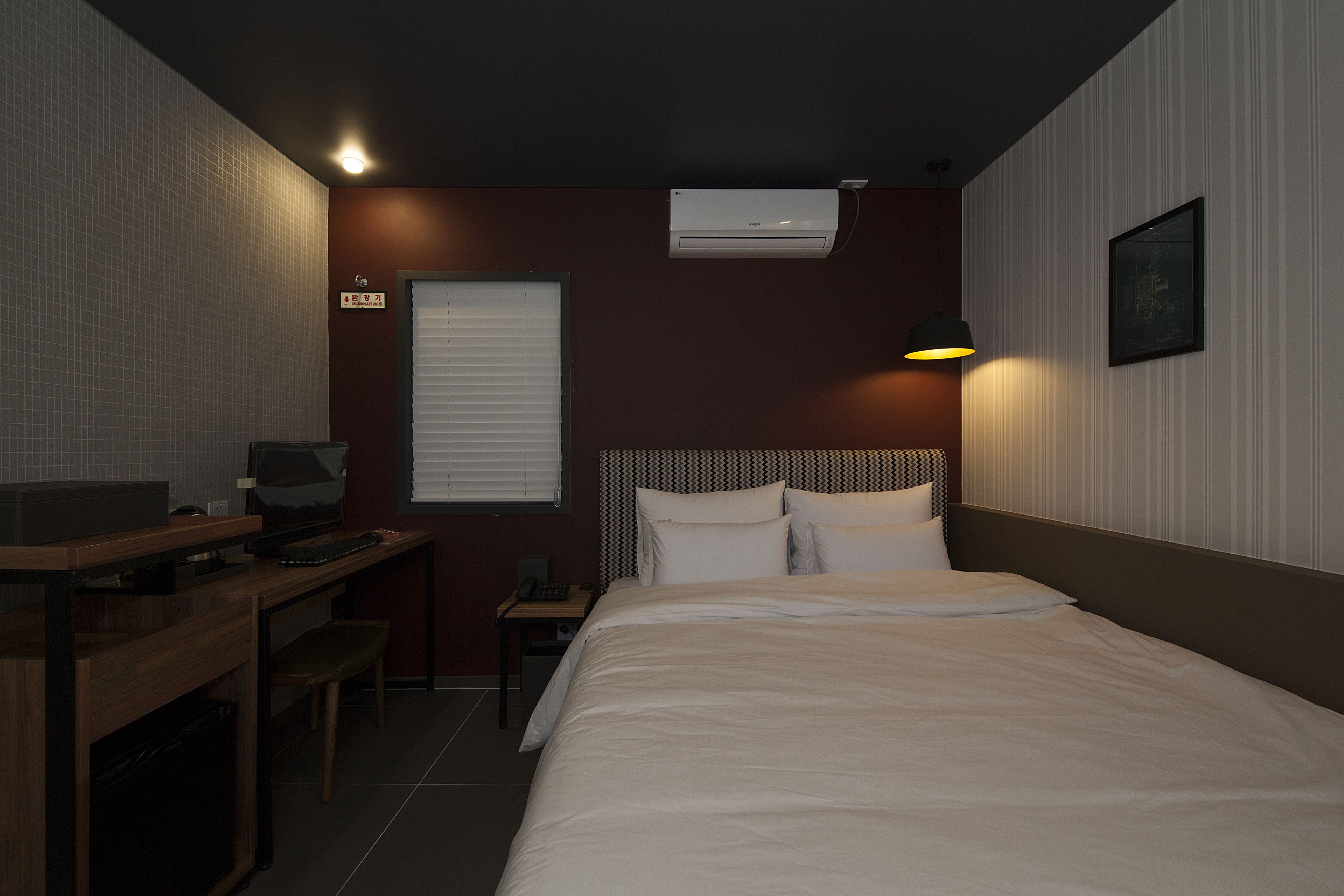 Une chambre d’hôtel avec un lit, un bureau, une chaise et une petite table avec une lampe.