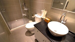 A modern bathroom with a glass shower enclosure, a toilet, a sink, and a mirror. - leaf hostel (Tainan)