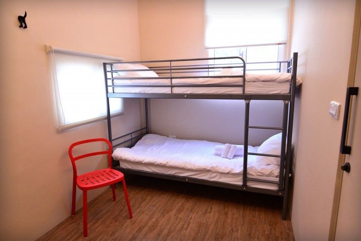 A bunk bed room with a red chair, a window with blinds, and a door.