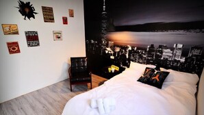 A hotel room with a bed, a chair, a desk, and a cityscape mural on the wall. - leaf hostel (Tainan)