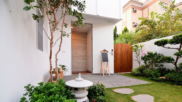 A modern outdoor space with a wooden door, a small table, and a garden area with stepping stones and greenery. - leaf hostel (Tainan)