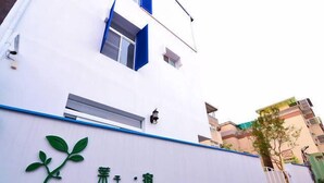 A building with a white facade, a blue window frame, and a green sign with Chinese characters. - leaf hostel (Tainan)