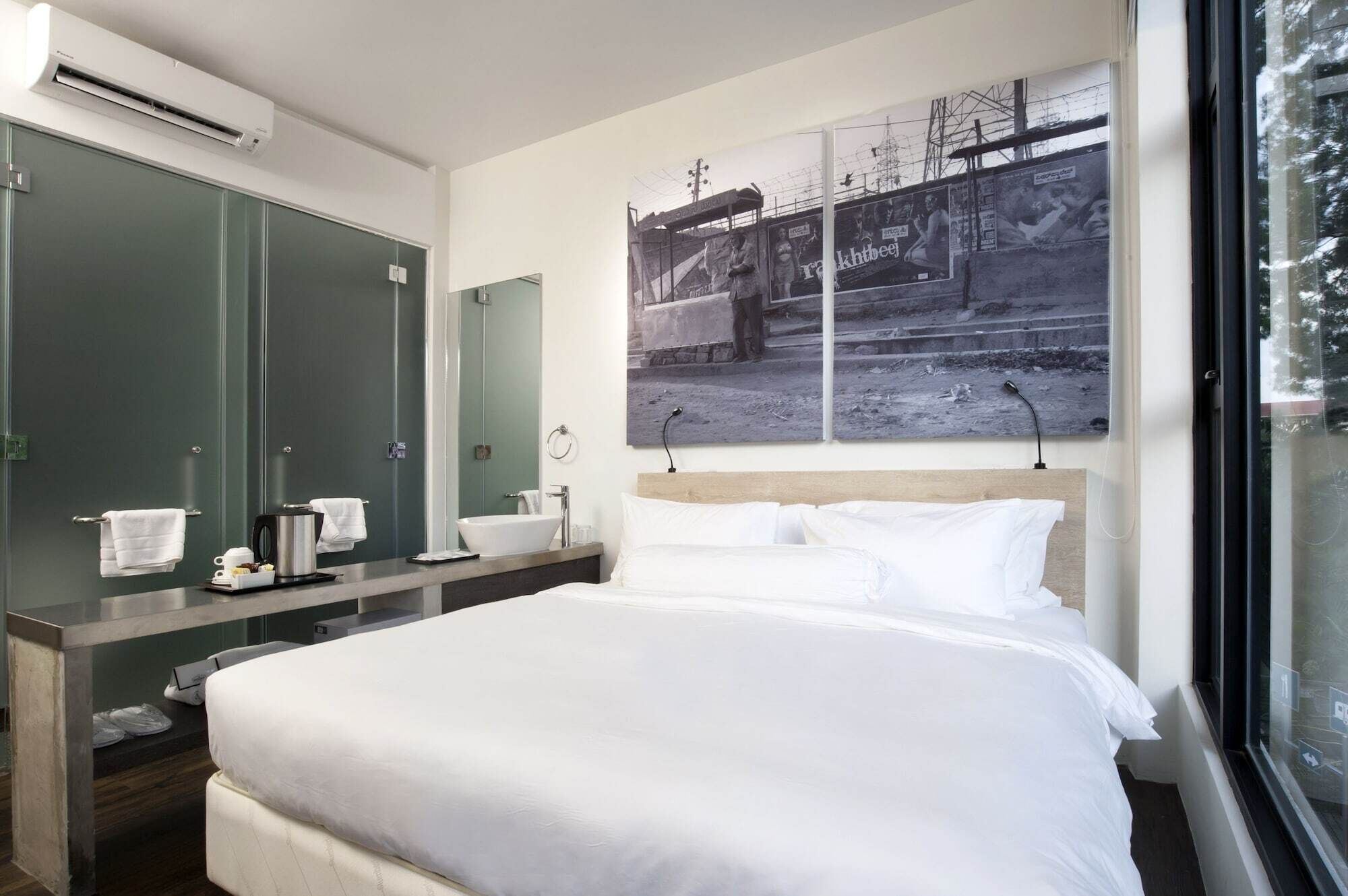 A modern hotel room with a large bed, a vanity with a mirror, a sink, and a window with a view of a building.