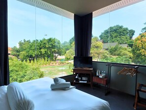 A hotel room with a large bed, a TV, a desk with a kettle, and a view of a park.