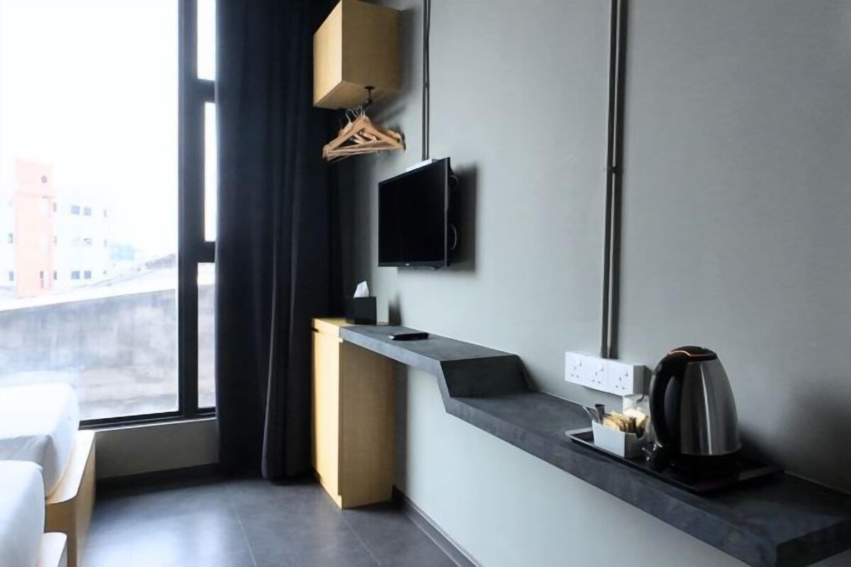 Una habitación de hotel moderna con un ventanal grande, un televisor de pantalla plana en la pared, un escritorio pequeño con una tetera y un perchero.