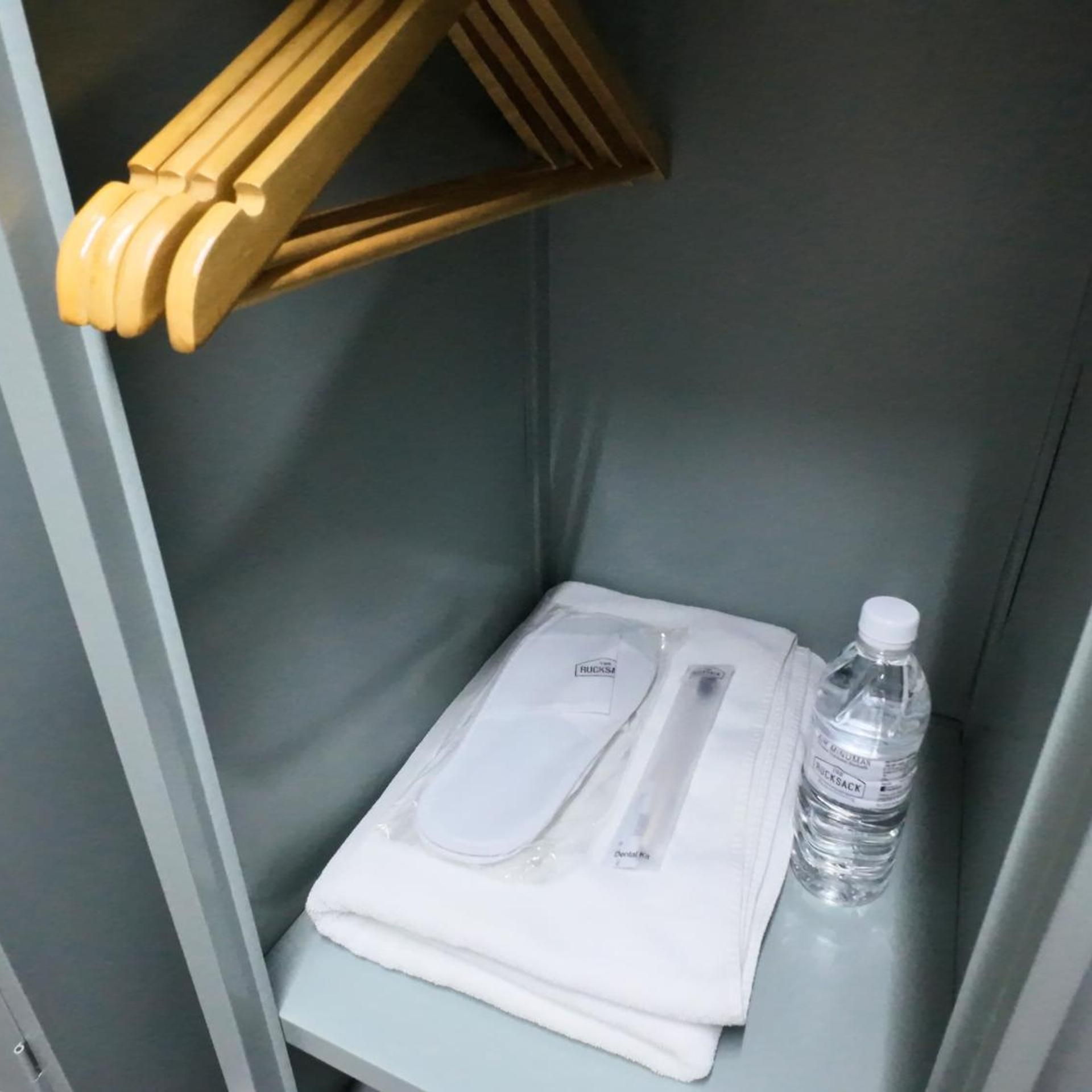 Een hoek van een kamer met een houten plank, een opgevouwen witte handdoek, een tandenborstel en een fles water.