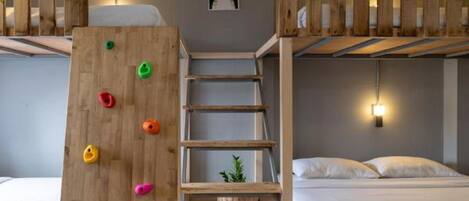 Habitación con literas, una pared de escalar, una escalera y una planta pequeña en el suelo.