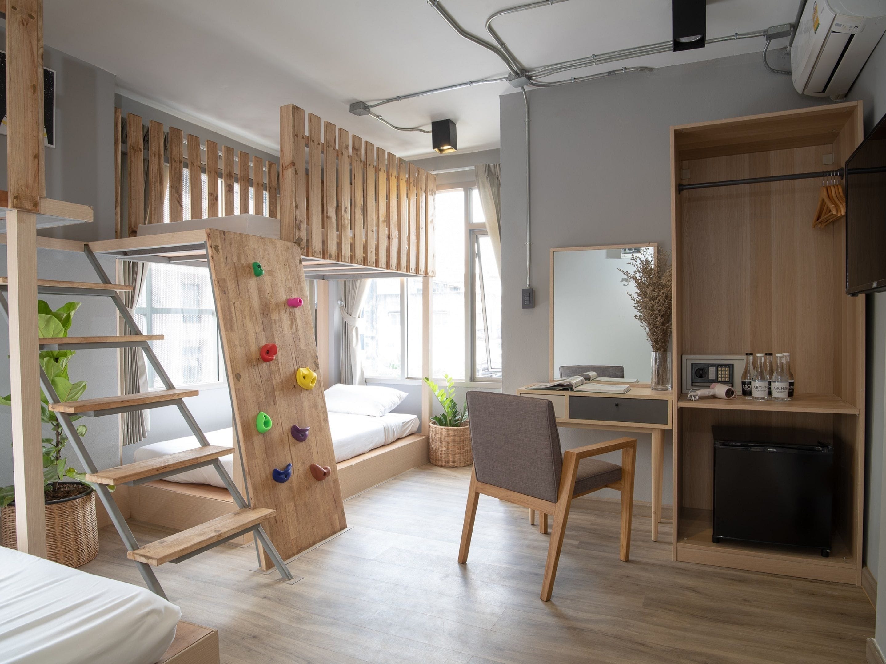 A modern room with a bunk bed, a desk, a chair, a small fridge, and a climbing wall.
