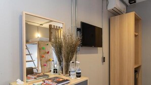 Una habitación moderna con un escritorio de madera, un espejo, un televisor montado en la pared y un armario de madera.