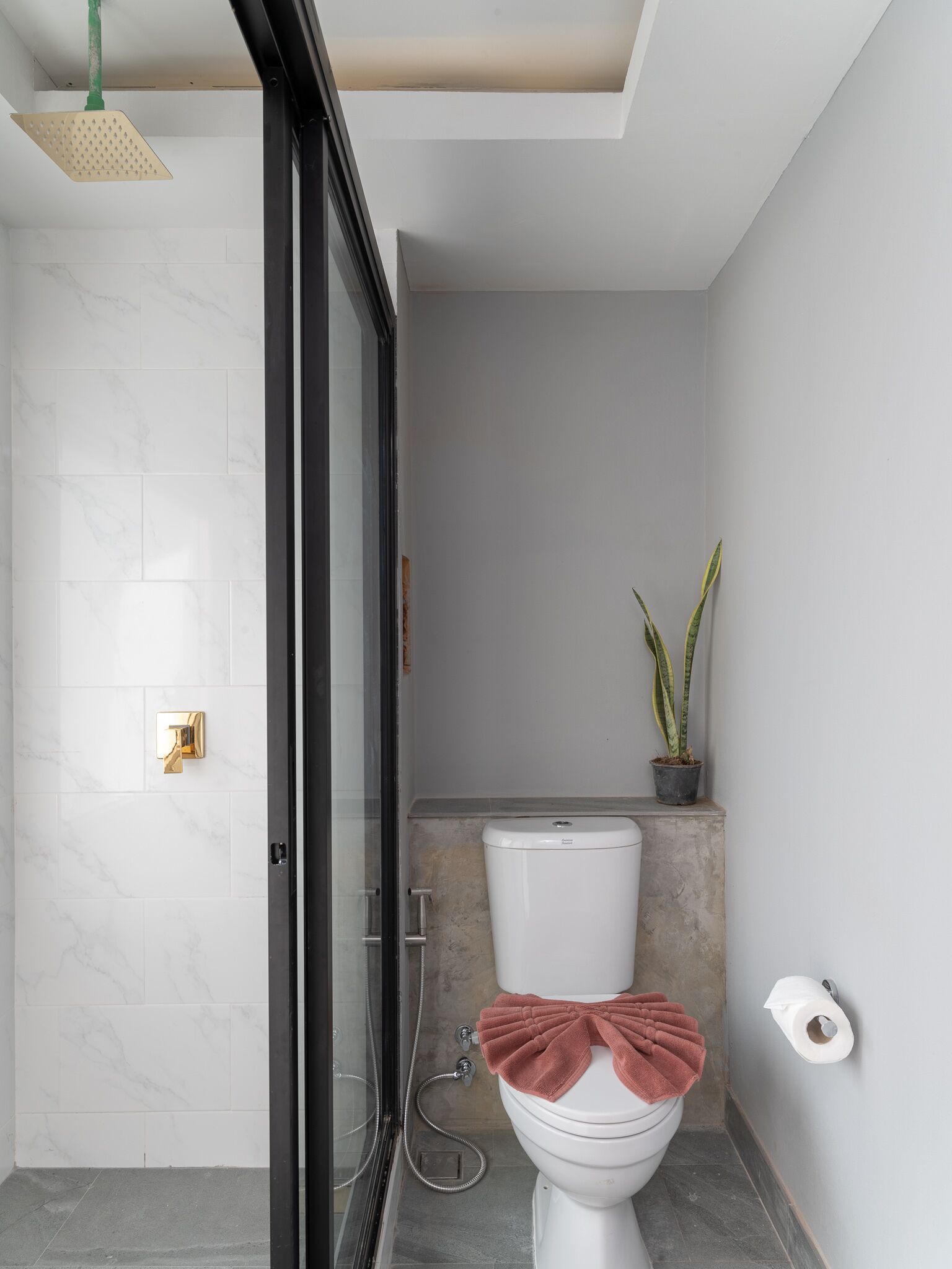 A modern bathroom with a glass shower door, a toilet with a towel on it, and a potted plant.