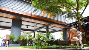 An outdoor area with a covered walkway, greenery, and a statue. - Le Terrarium Hotel (Chiang Rai)