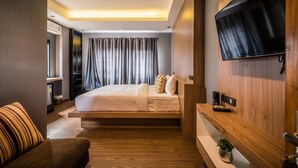 A modern hotel room with a bed, a TV mounted on the wall, a wooden bench, and a small table with a plant. - Le Terrarium Hotel (Chiang Rai)