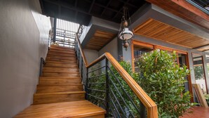 A wooden staircase with a black railing, leading to a second-floor landing with a hanging light fixture. - Le Terrarium Hotel (Chiang Rai)