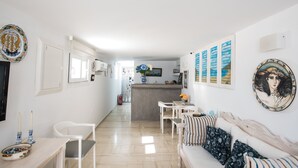 A modern, well-lit living area with a sofa, chairs, a small table, and a kitchen area in the background. - Spanelis Hotel (Mykonos)