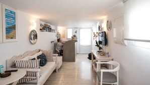 A modern, well-lit living area with a sofa, a dining table, and a kitchen in the background. - Spanelis Hotel (Mykonos)