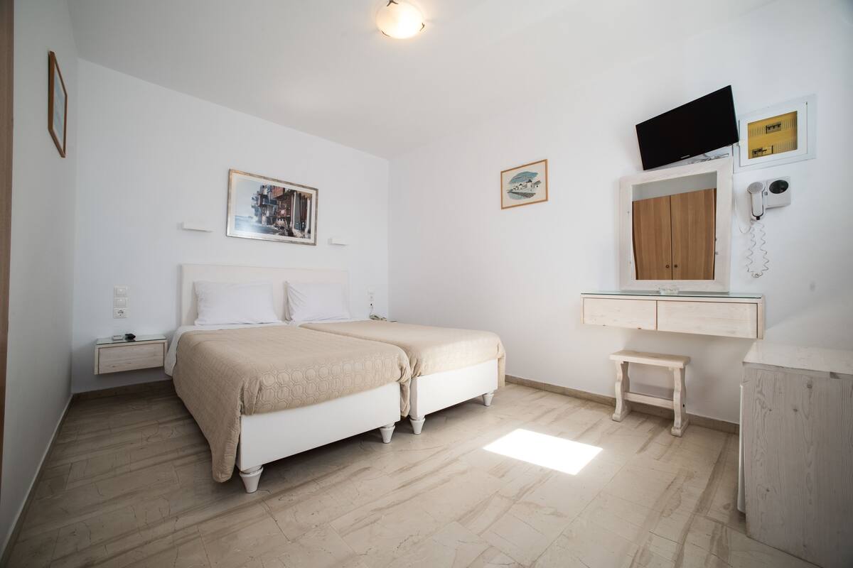 A bedroom with two beds, a bedside table, a small stool, a TV, a mirror, and a wall-mounted heater.