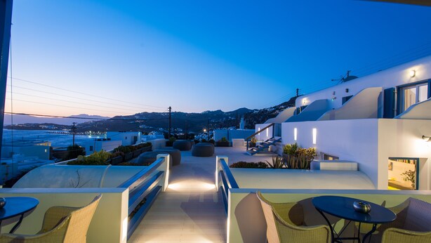 A rooftop terrace with outdoor seating, a view of the sea, and modern architecture. - Spanelis Hotel (Mykonos)
