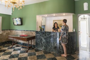 A reception area with a marble counter, a wooden table with a red folder, and a chandelier.