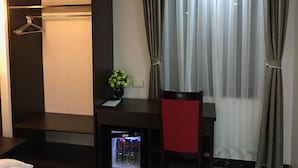 A compact room with a dark-colored wardrobe, a small table with a vase of green flowers, a red chair, and a mini-fridge. - Sapa Memory Hotel (Sa Pa)