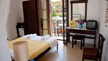 A bedroom with a bed, a desk, a chair, a television, and a balcony with a view of the countryside.