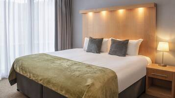 A hotel room with a large bed, a bedside table with a lamp, and a view through sheer curtains.