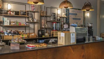 Mostrador de una cafetería con diversas bebidas, pasteles y un anuncio que ofrece un 10% de descuento para clientes que traigan su propio vaso.