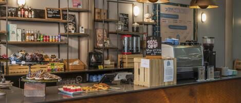 A coffee shop counter with a variety of beverages, pastries, and a sign offering a 10% discount for customers bringing their own cup.