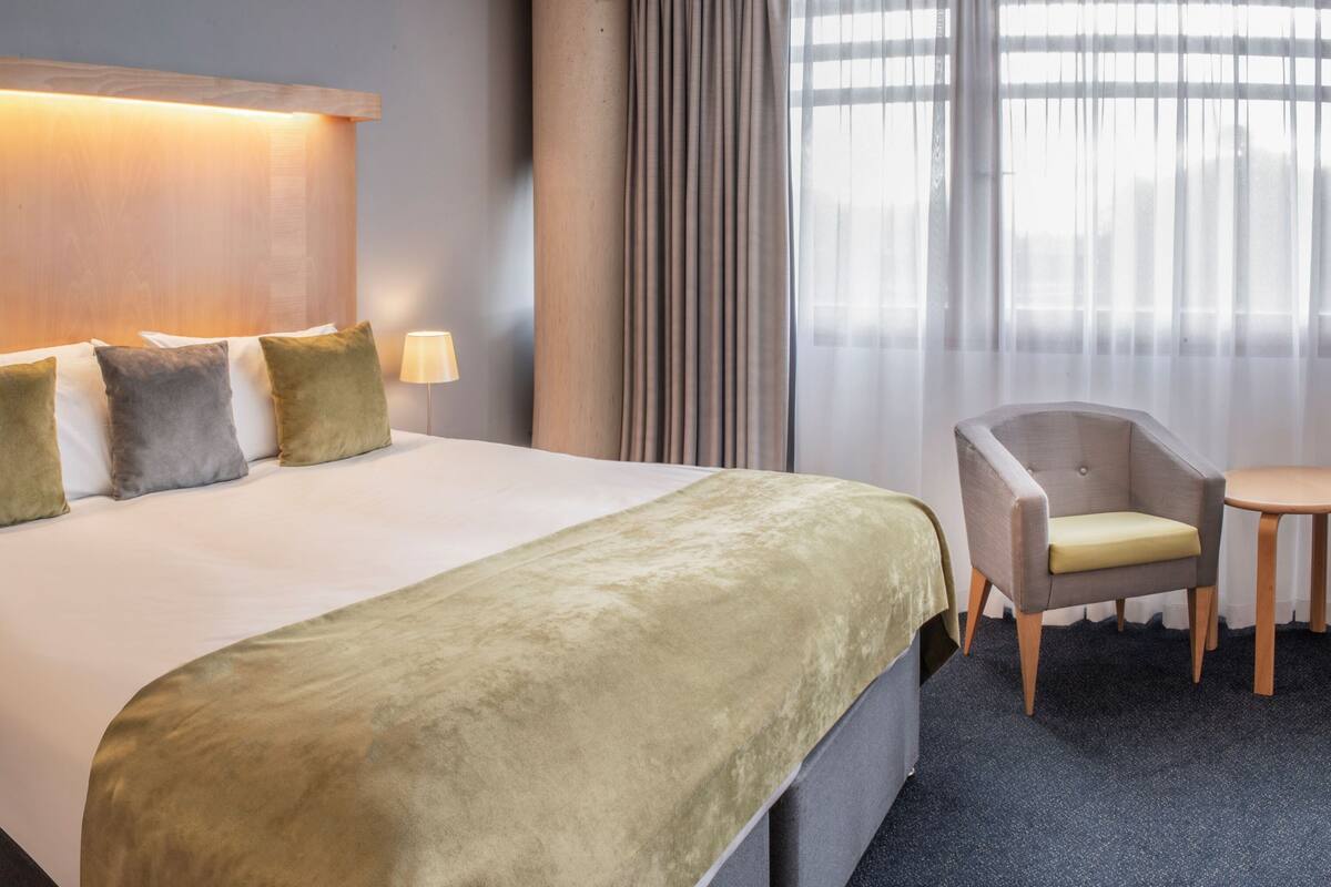 A hotel room with a large bed, a bedside table, a chair, and a small table.