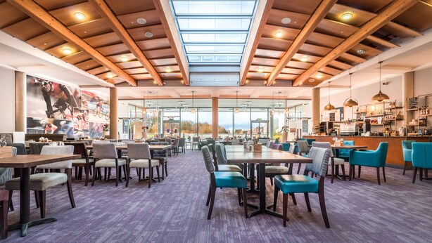 A spacious restaurant with high ceilings, large windows, and a variety of seating options including tables and chairs. - The Jubilee Hotel & Conferences (Nottingham)