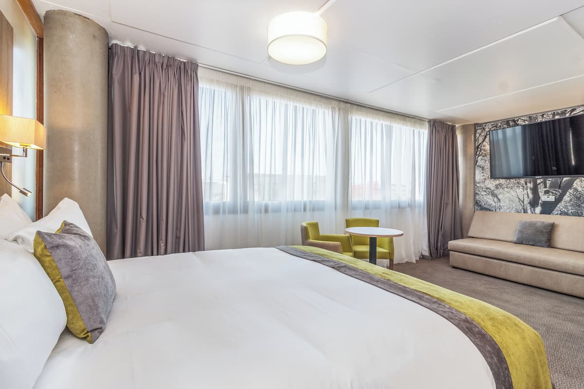 A hotel room with a large bed, a sofa, a small table, and a TV mounted on the wall.