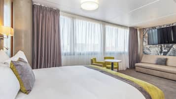 A hotel room with a large bed, a sofa, a small table, and a TV mounted on the wall.