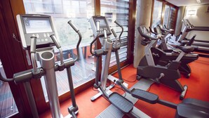 A gym with various cardio machines, a control panel, and large windows with a view of buildings outside. - The Jubilee Hotel & Conferences (Nottingham)
