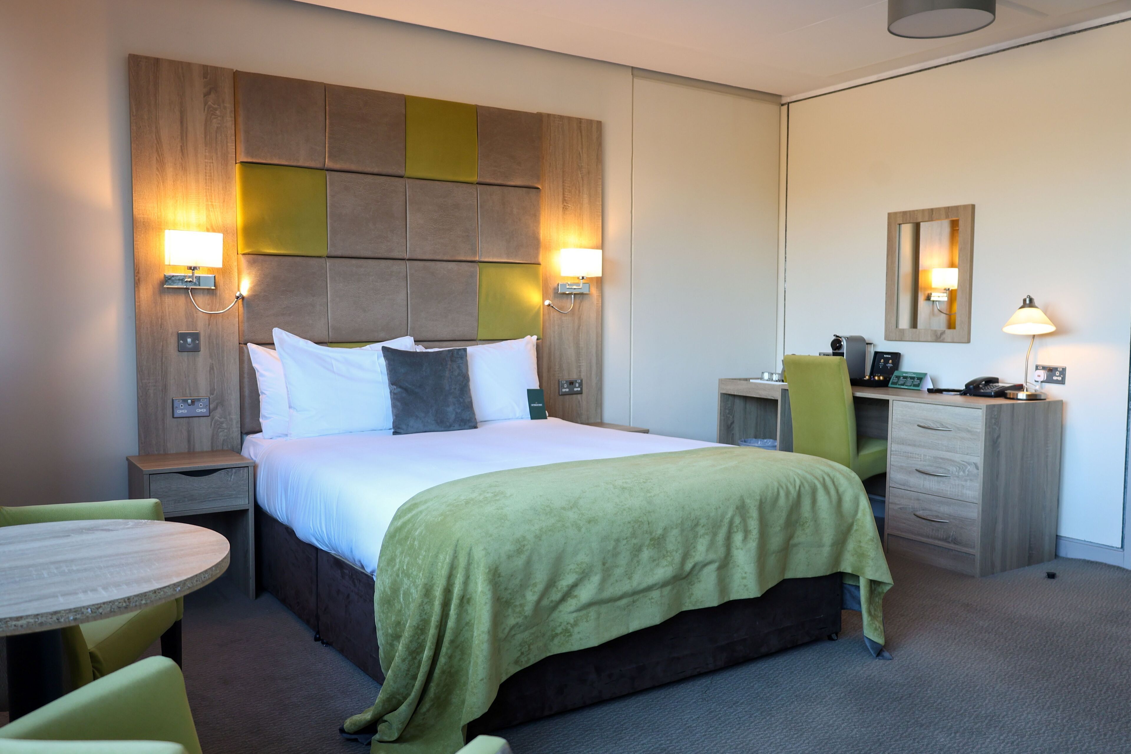A hotel room with a bed, bedside tables, a desk, a chair, and a round table.