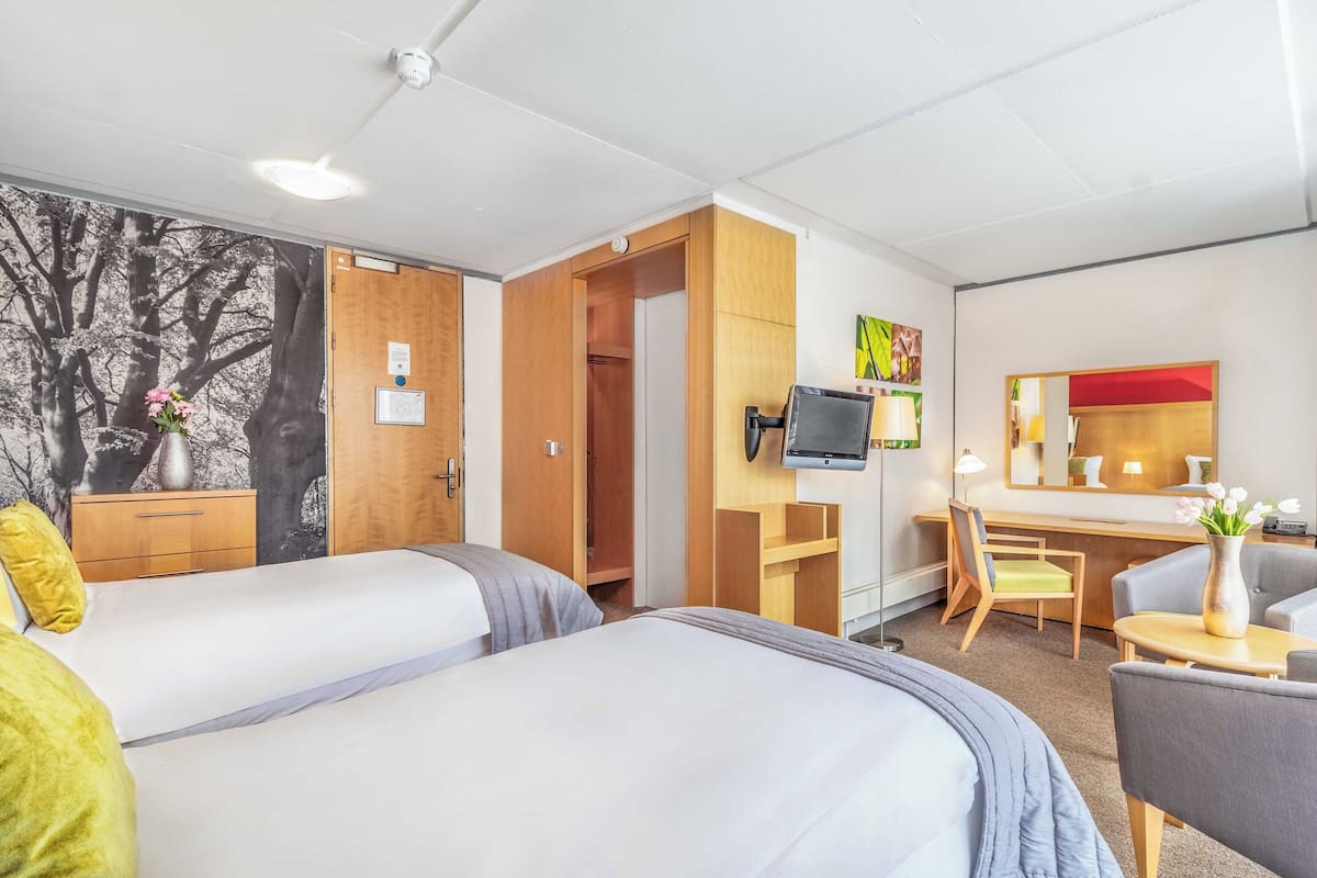 A hotel room with two beds, a desk, a chair, a TV, and a wardrobe.