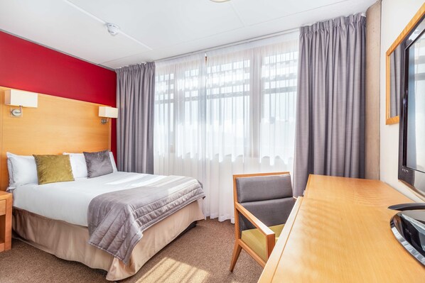 A hotel room with a bed, a desk, a chair, and a TV.