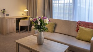 A modern hotel room with a sofa, a small table, a desk, and a window with curtains. - The Jubilee Hotel & Conferences (Nottingham)