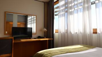 A hotel room with a bed, a desk with a television, a mirror, and a window with curtains.