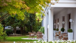 A covered outdoor seating area with wicker chairs and potted plants, surrounded by lush greenery. - Hotel Salus Terme (Abano Terme)