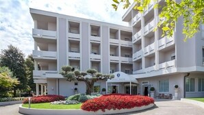 A multi-story hotel with a central entrance, surrounded by landscaped gardens and a large tree. - Hotel Salus Terme (Abano Terme)
