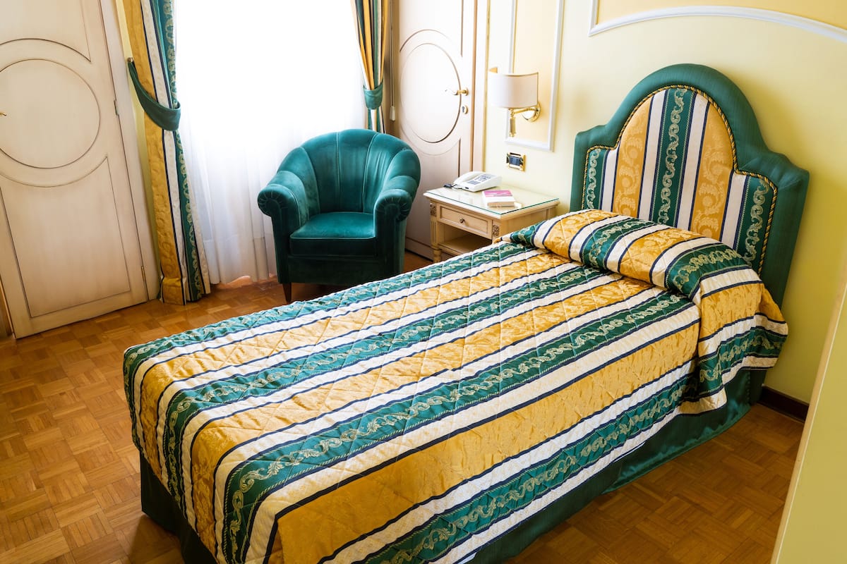 Een hotelkamer met een bed, een stoel, een nachtkastje en een lamp.