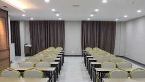 Un salón de conferencias con filas de sillas y mesas, un panel de pared de madera y un amplio ventanal con cortinas.